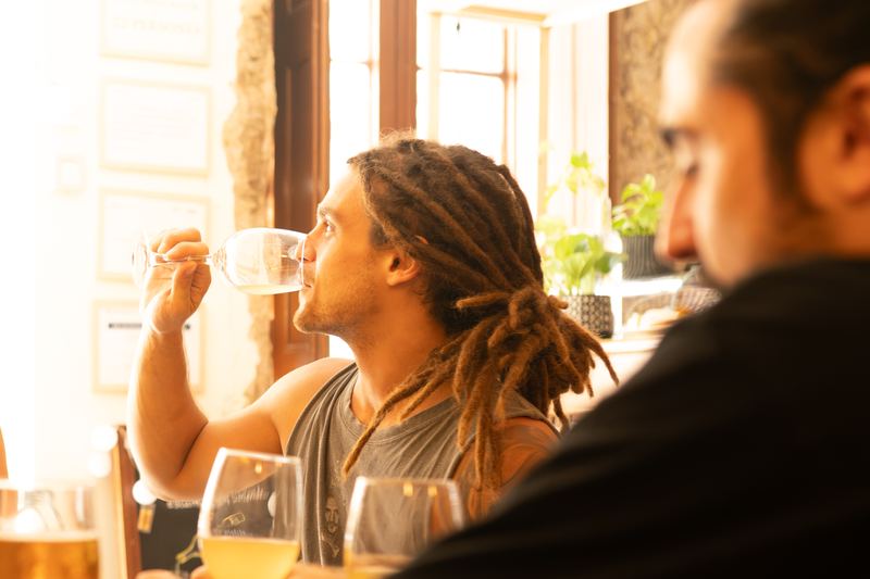 Un cliente bebe una copa de vino blanco junto a una ventana luminosa