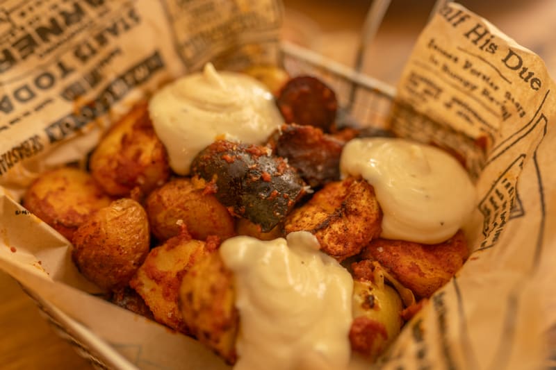 Primer plano de patatas pateras: patatas especiadas con trozos de embutido y mayonesa de ajo en una cesta forrada con papel de periódico