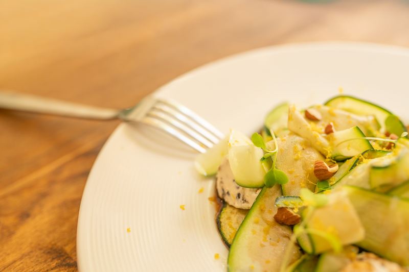 Plato de láminas de calabacín con almendras tostadas y ralladura de limón sobre una mesa de madera