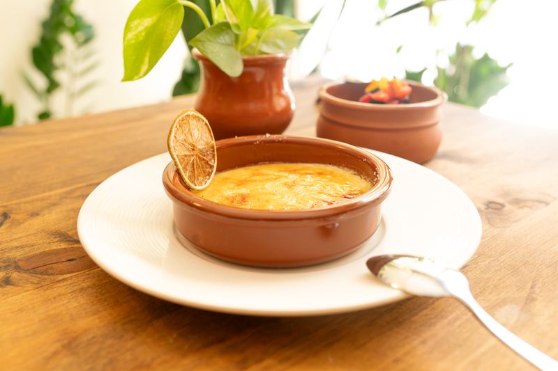 Postre gratinado en cazuela de barro con una rodaja de lima deshidratada, sobre una mesa de madera con plantas